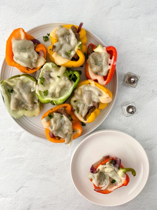 image of prepared philly cheesesteak stuffed peppers on white plate with a small white plate with one pepper and salt and pepper shakers