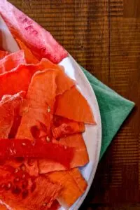 watermelon jerky in white bowl on top of green tea towel and wooden boards