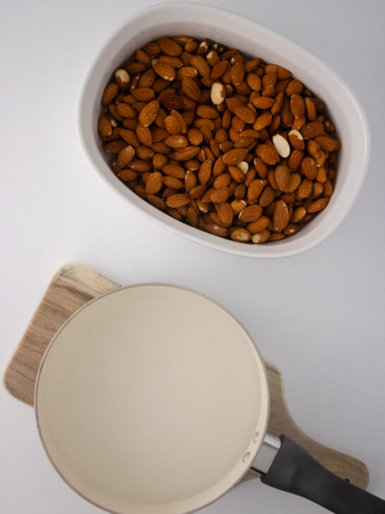 raw almonds on a glass dish with a pot of boiling water on a cutting board