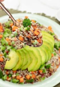 broccoli quinoa salad with carrots and avocado on spoon with big bowl of quinoa salad in background