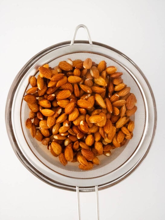 almonds straining in strainer over glass bowl after soaking in boiled water