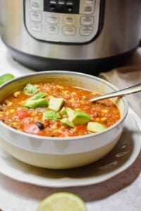 instant pot vegetable quinoa soup topped with avocado in bowl with instant pot in background and lime wedges