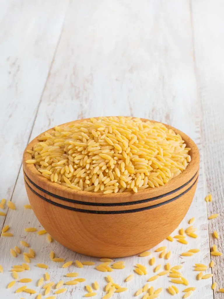 uncooked orzo in wooden bowl on top of white wooden planks