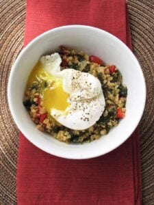 quinoa in bowl with veggies and poached egg with cracked pepper on red towel
