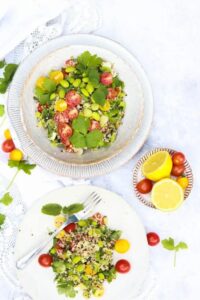 quinoa tabbouleh salad with edamame and lemon on plates on white marble counter