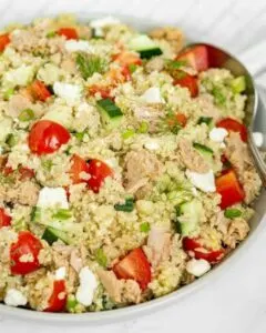 quinoa tuna salad with tomato and cucumber in white bowl with spoon