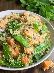 thai quinoa salad topped with snowpeas in white bowl on wooden table