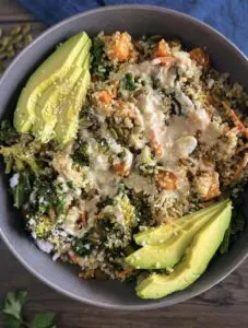 warm quinoa salad topped with sesame dressing and avocado slices in a grey bowl