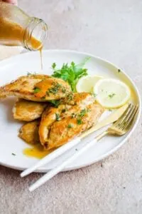 chicken limone on white plate with sauce drizzling over chicken breasts