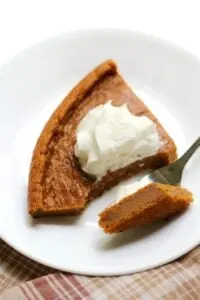 slice of crustless sweet potato pie topped with whipped cream on white plate with fork