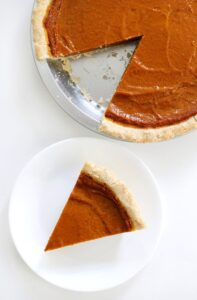 gluten free pumpkin pie in pie pan with slice cut out and on a plate.