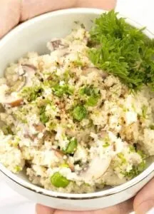 cauliflower risotto with parsley and mushrooms in white bowl held by two hands