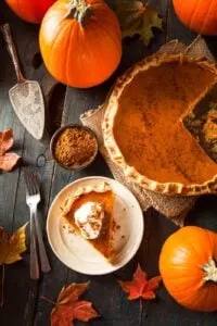 healthy pumpkin pie with slice cut out and topped with whipped cream and pumpkins and leaves in background