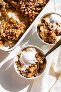 gluten free apple crisp in white casserole dish and in two small bowls topped with ice cream
