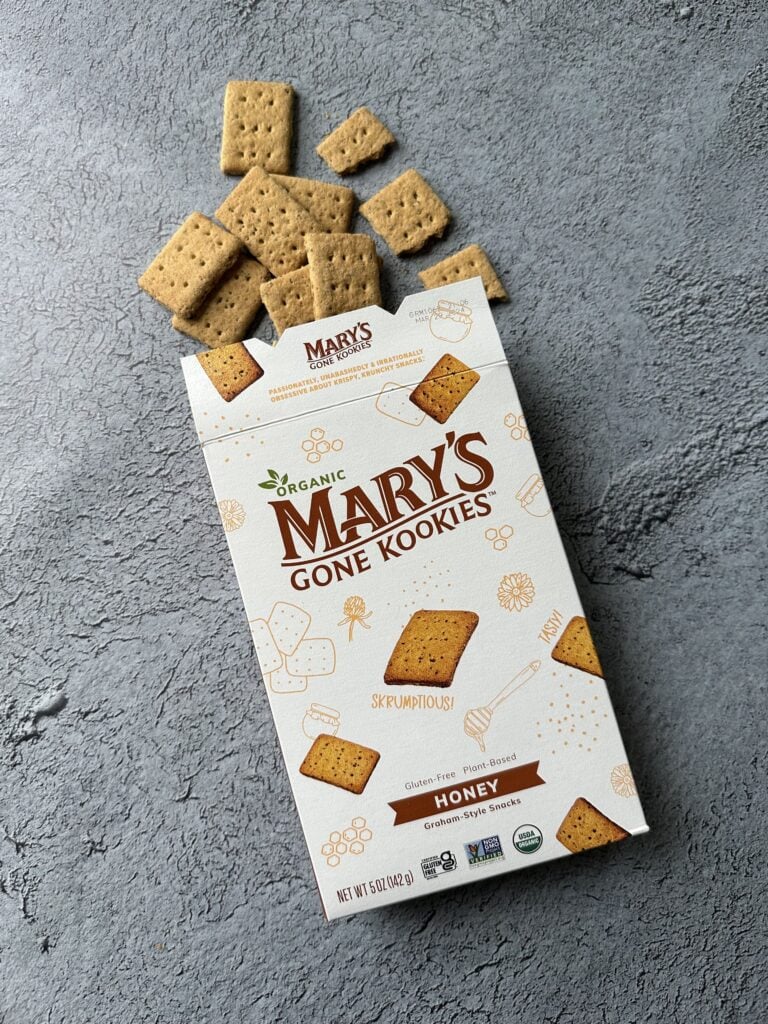 box of mary's gone kookies honey graham-style snacks on concrete with crackers spilling out of the box