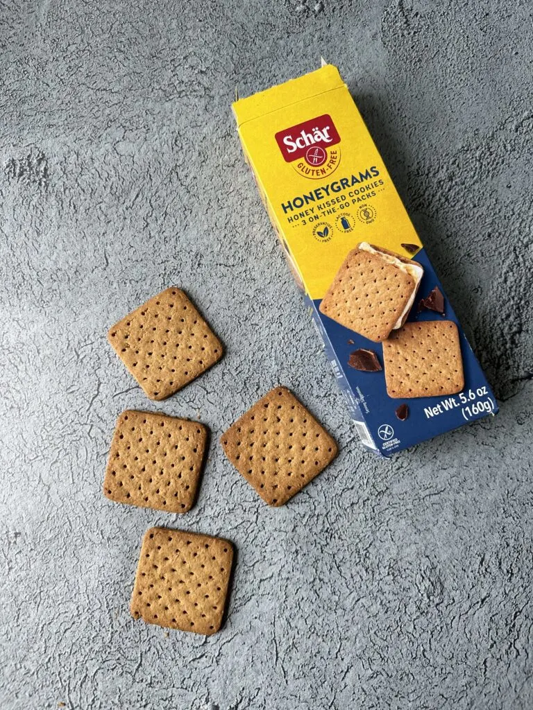 box of schar honeygrams gluten free graham crackers on concrete with four graham crackers next to the box