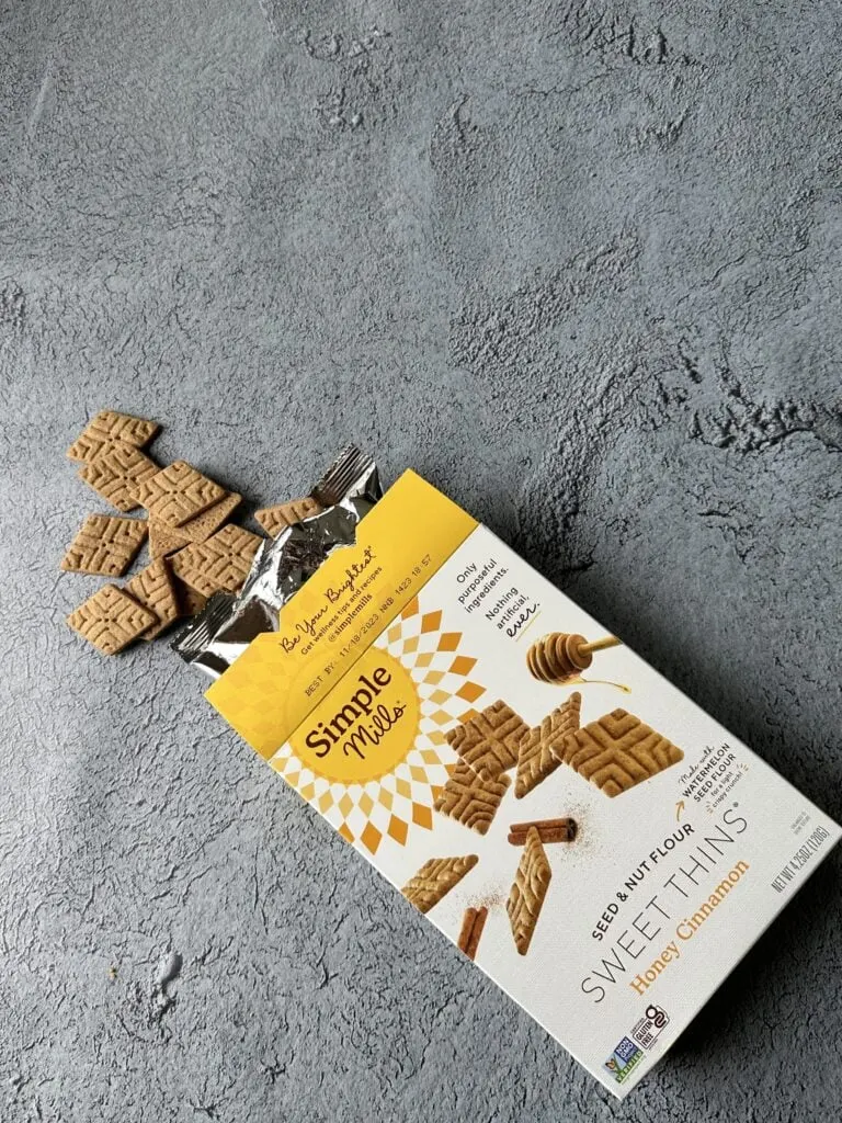 box of simple mills honey cinnamon sweet thins on concrete with crackers spilling out of the box