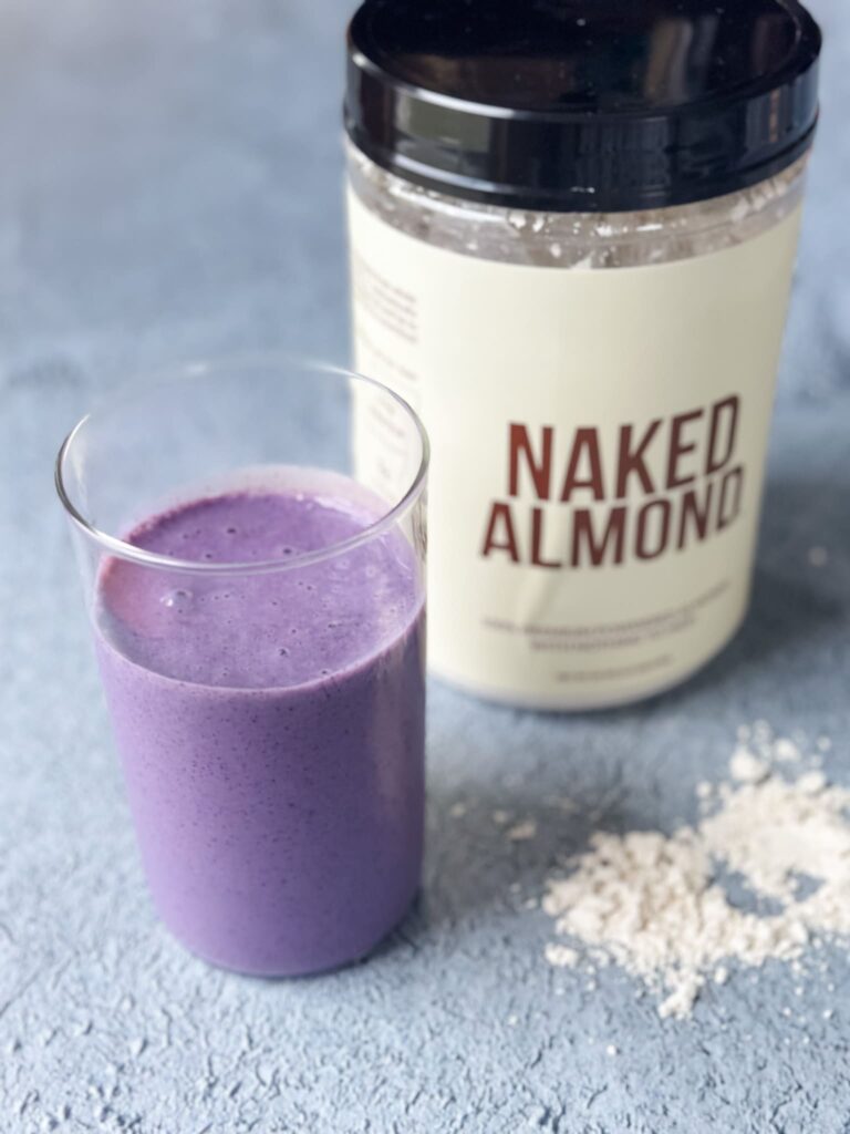 gluten free vegan berry protein shake in glass with naked almond protein powder by naked nutrition in background