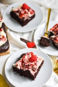 slices of gluten free vegan chocolate cake topped with frosting, raspberries, and chocolate on white plates