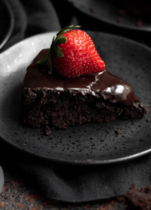 gluten free vegan flourless chocolate cake on black plate topped with a strawberry