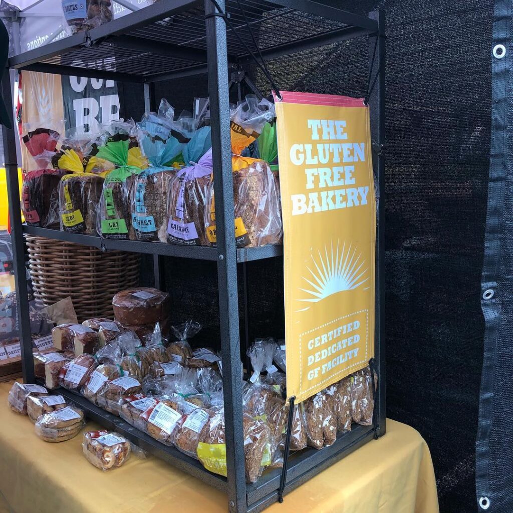 A stand with loaves of gluten free bread and baked goods with a sign that reads 'The Gluten Free Bakery Certified Dedicated GF Facility' at the Troy Waterfront Farmers Market