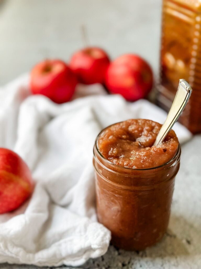 cinnamon brown sugar applesauce in mason jar with apples and white tea towel and amber jug in background