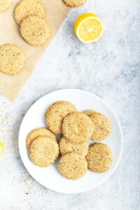 gluten free vegan tahini cookies on white plate set on stone counter with a lemon