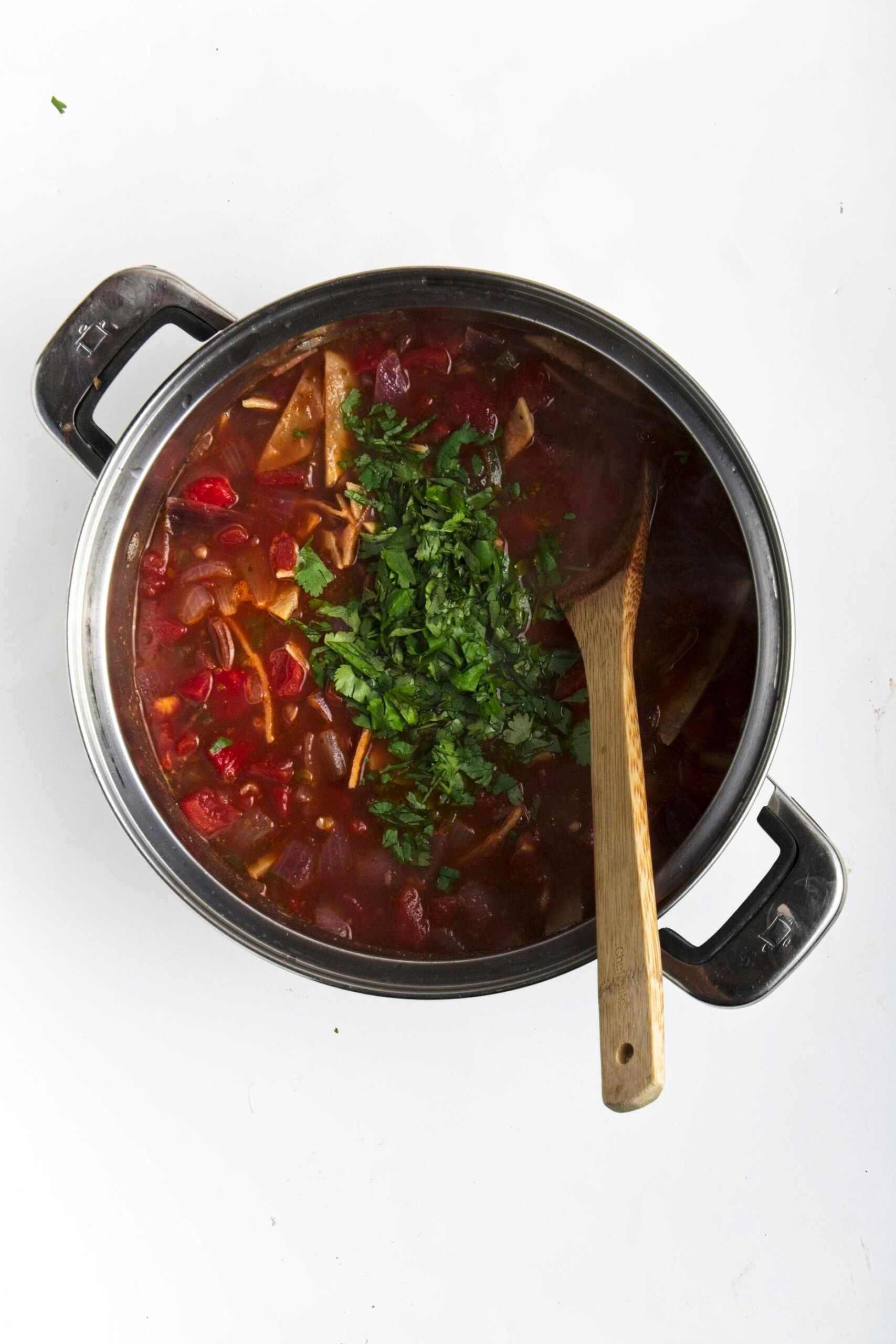 A pot of vegetarian tortilla soup with a wooden spoon and garnished with cilantro
