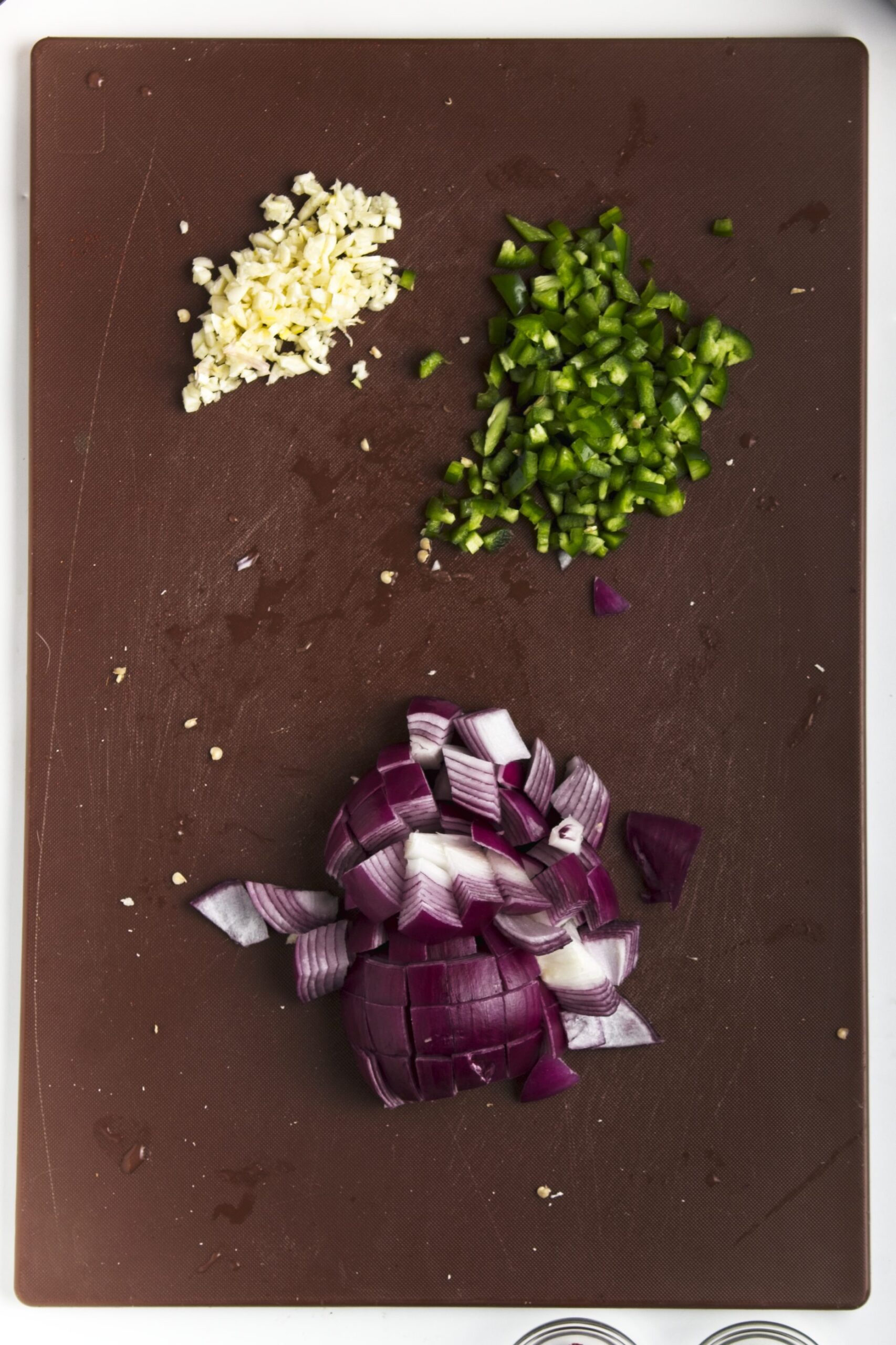 Chopped garlic, chopped jalapeño and chopped red onion on a cutting board
