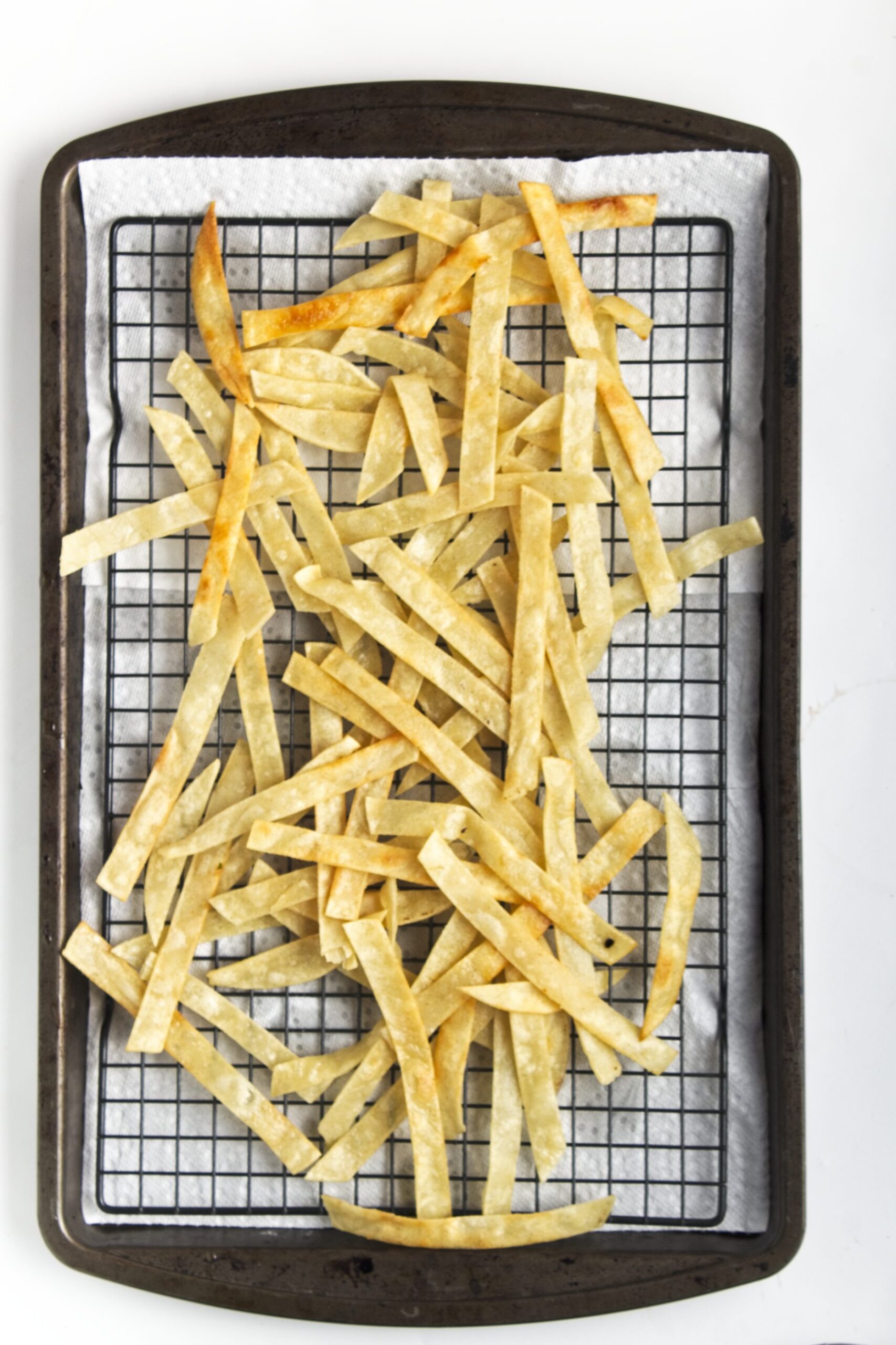 Fried crispy tortilla strips sitting on a baking sheet lined with paper towel