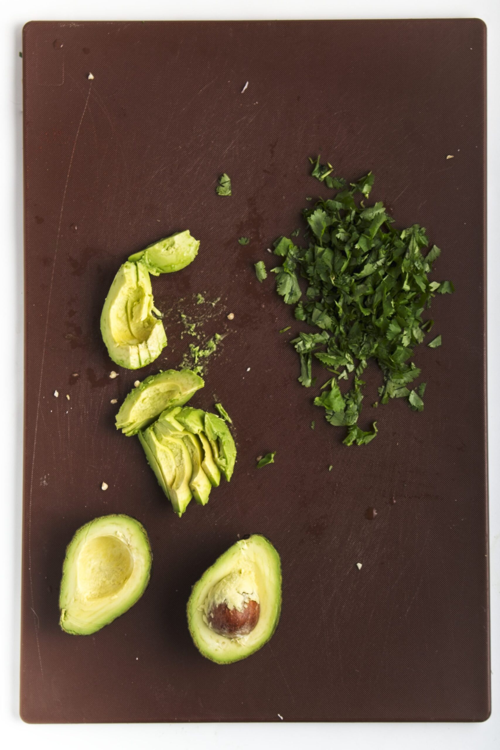 Sliced avocado and chopped cilantro sitting on a brown cutting board