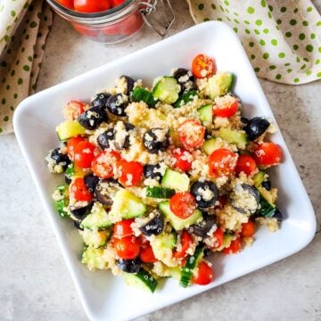 gluten free vegan mediterranean quinoa salad on white plate with bowl of tomatoes