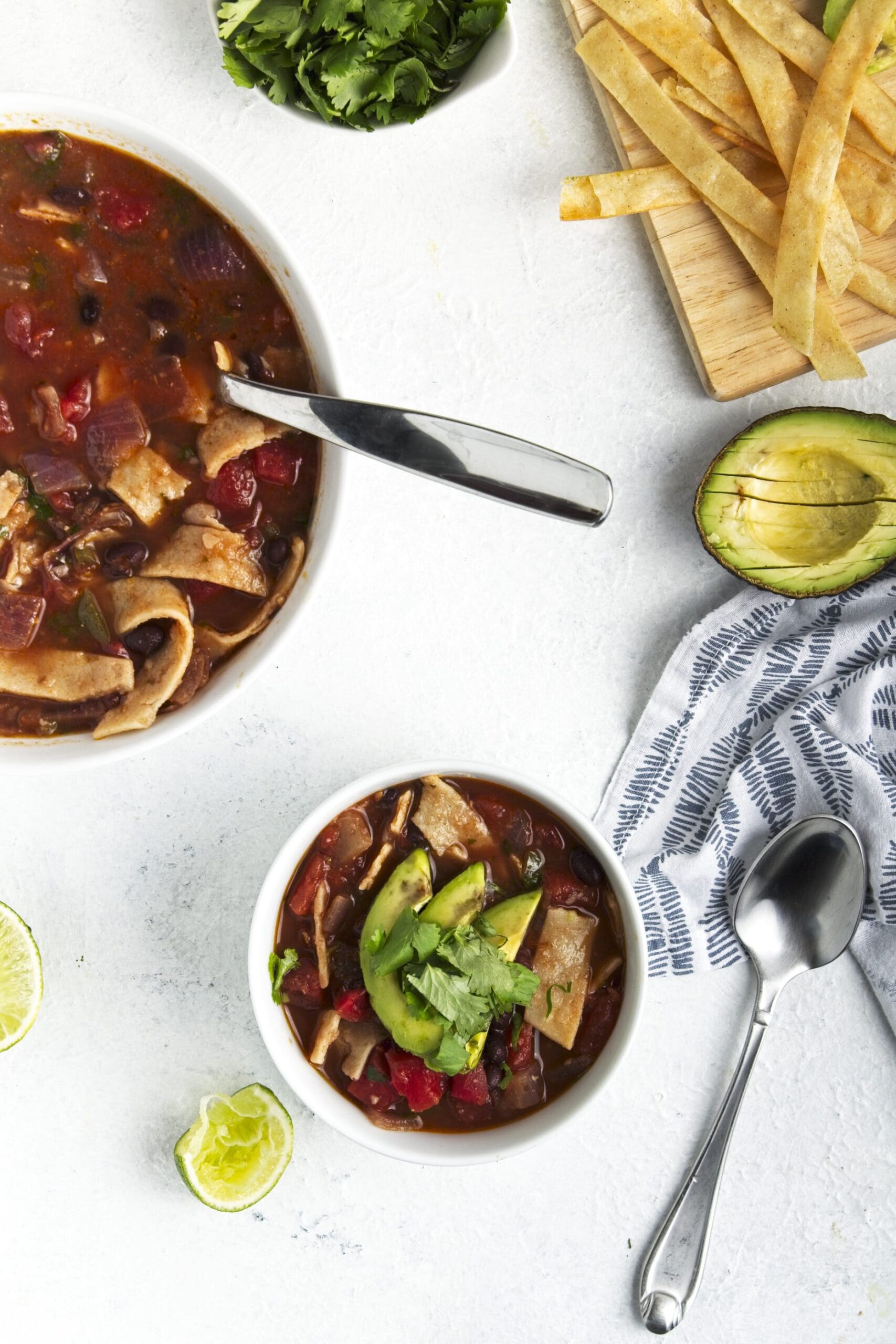 Gluten Free Vegetable Tortilla Soup in white bowls with spoons with limes, avocados, and crispy tortilla strips