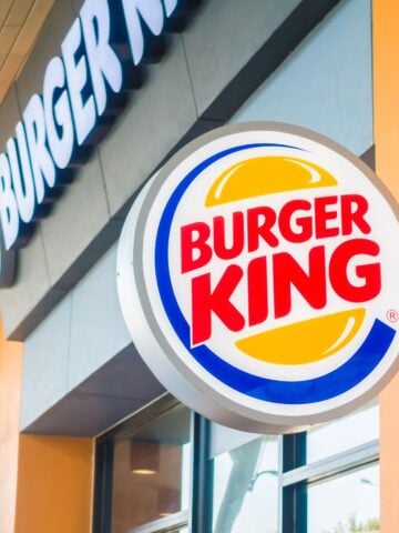 The outside of a Burger King restaurant with the logo in focus in the forefront and the restaurant blurred in the background