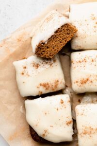 healthy pumpkin bar squares with frosting and cinnamon on parchment paper