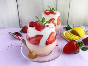 strawberry yogurt parfaits in parfait classes with spoons and sliced strawberries and lemons