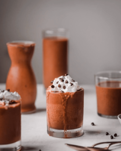 homemade vegan chocolate milkshakes in glasses topped with whipped cream and chocolate chips