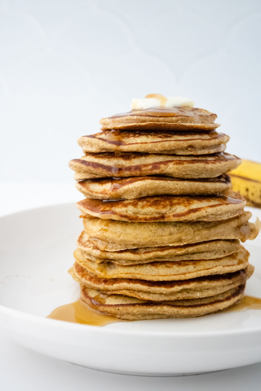 stack of gluten free banana oat blender pancakes on white plate topped with butter and syrup
