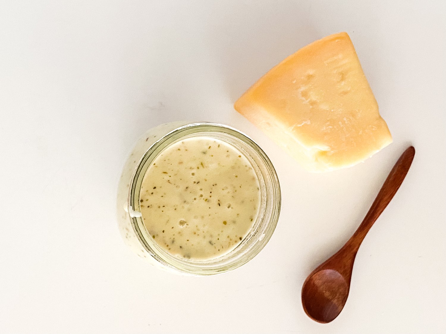 A top down photo of a jar of garlic parmesan wing sauce sitting beside a block of parmesan cheese and a wooden spoon