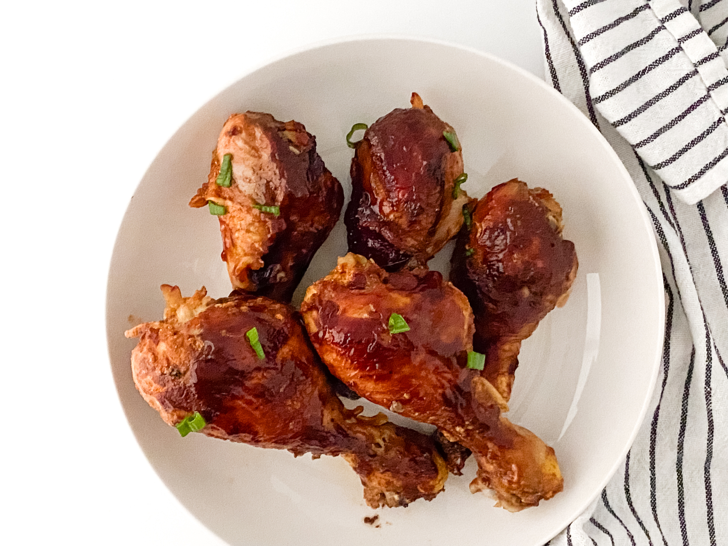 Flavorful Slow Cooker BBQ Chicken Drumsticks sitting on a white plate next to a black and white striped napkin