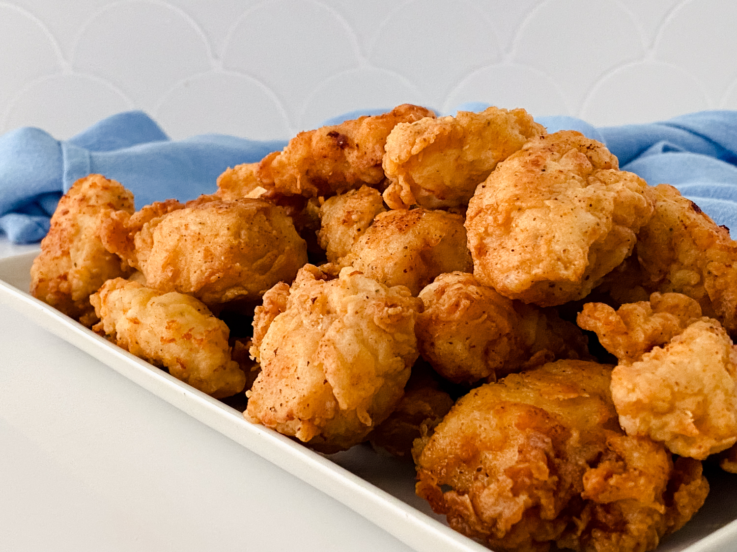 A close-up of cooked Gluten Free Chick-fil-A Chicken Nuggets sitting on a white rectangular serving tray with a blue cloth napkin in the background