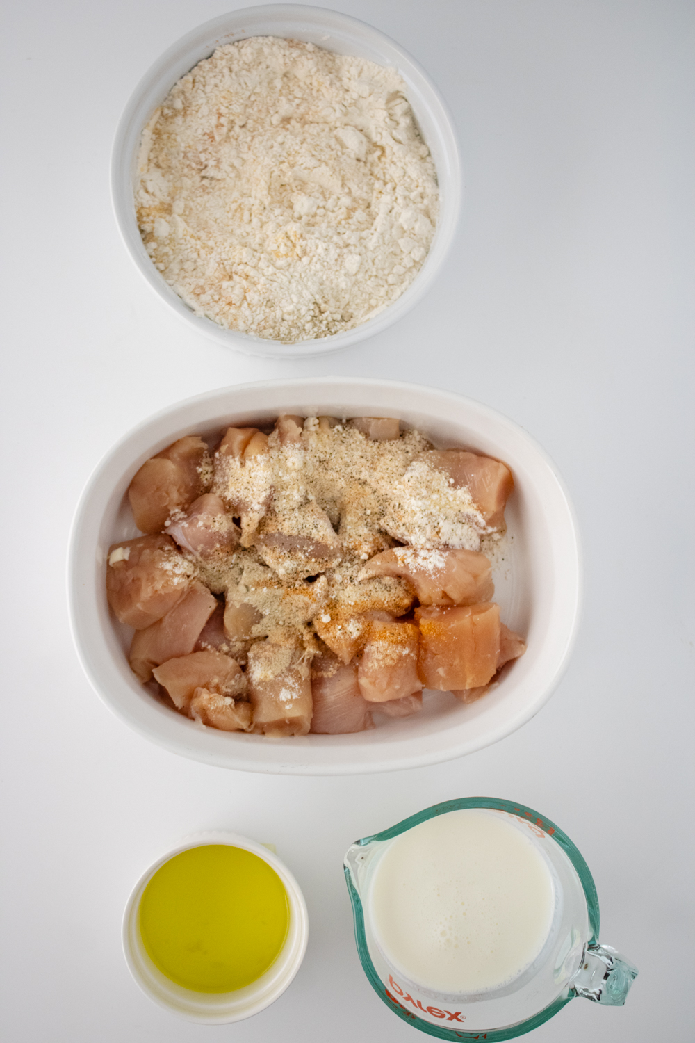 Seasonings have been dumped on top of raw chicken tenders. The other remaining ingredients for this Copycat Chick-Fil-A recipe are in bowls around the chicken.