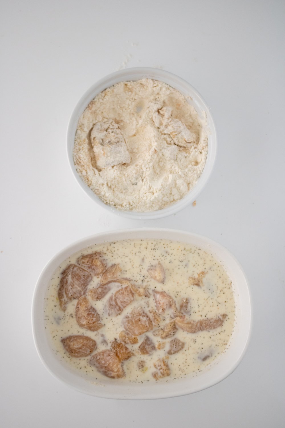 There are 2 white bowls on the counter. One has the seasoned chicken and the other has the dredge ingredients with a few pieces of chicken in it.