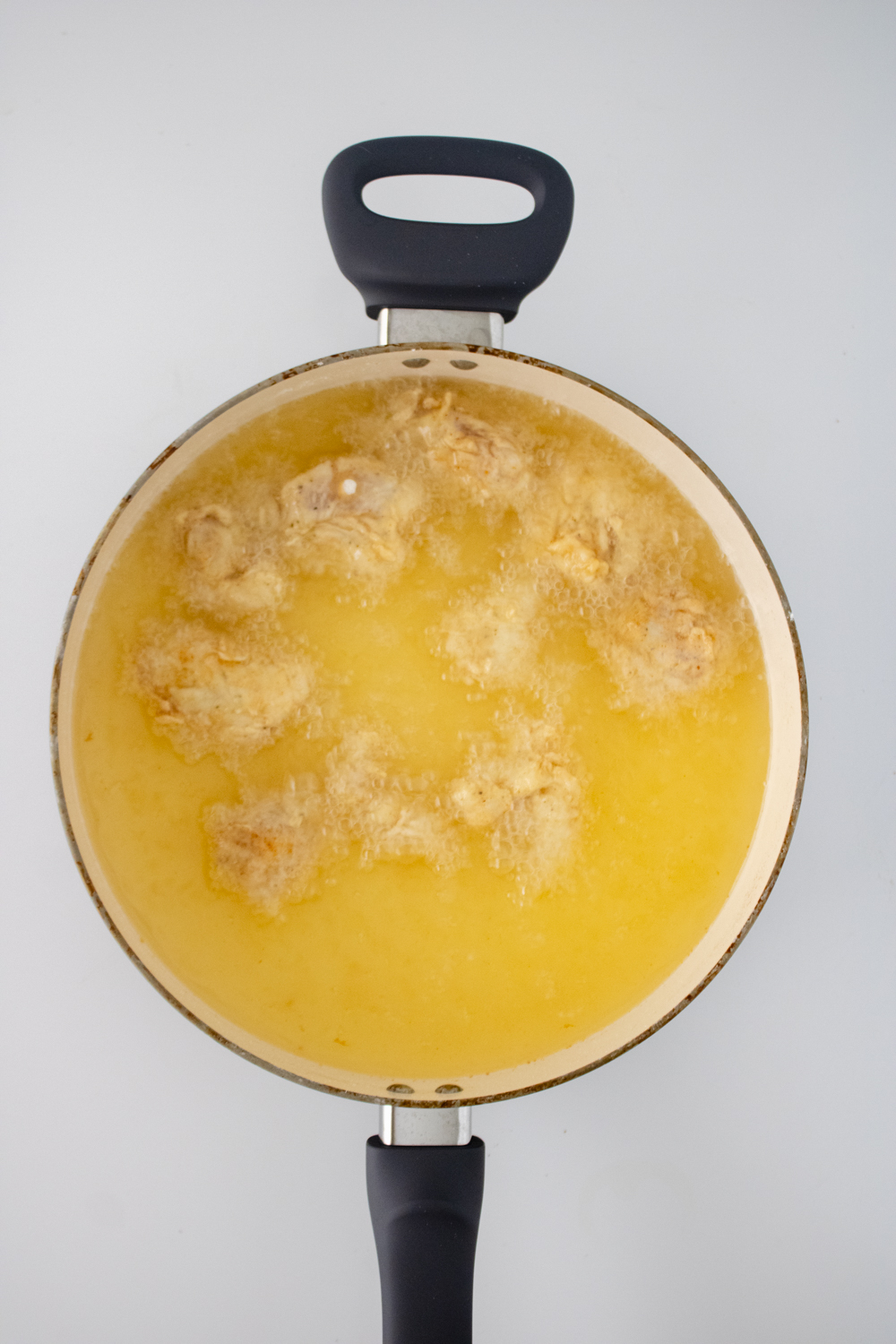 A pot with bubbling oil is frying a small batch of chicken tender pieces.