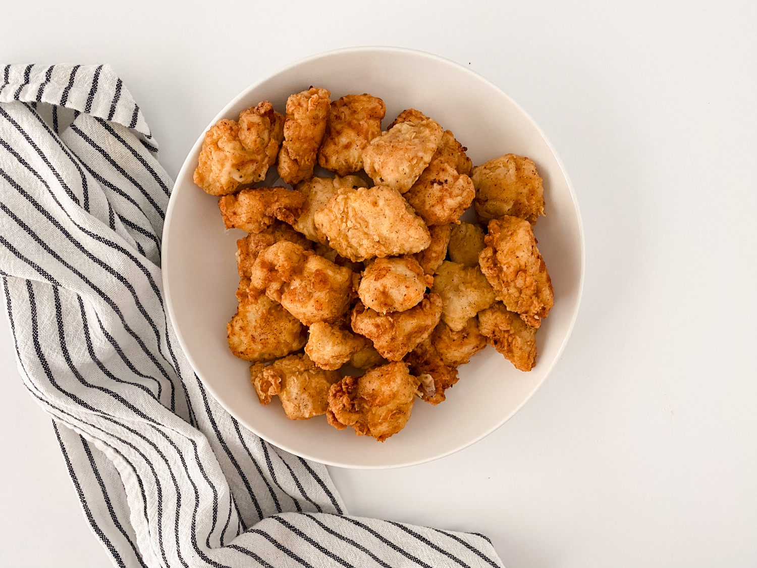 Crunchy Copycat Chick-fil-A Chicken Nuggets sitting in a white serving bowl beside a black and white striped cloth napkin