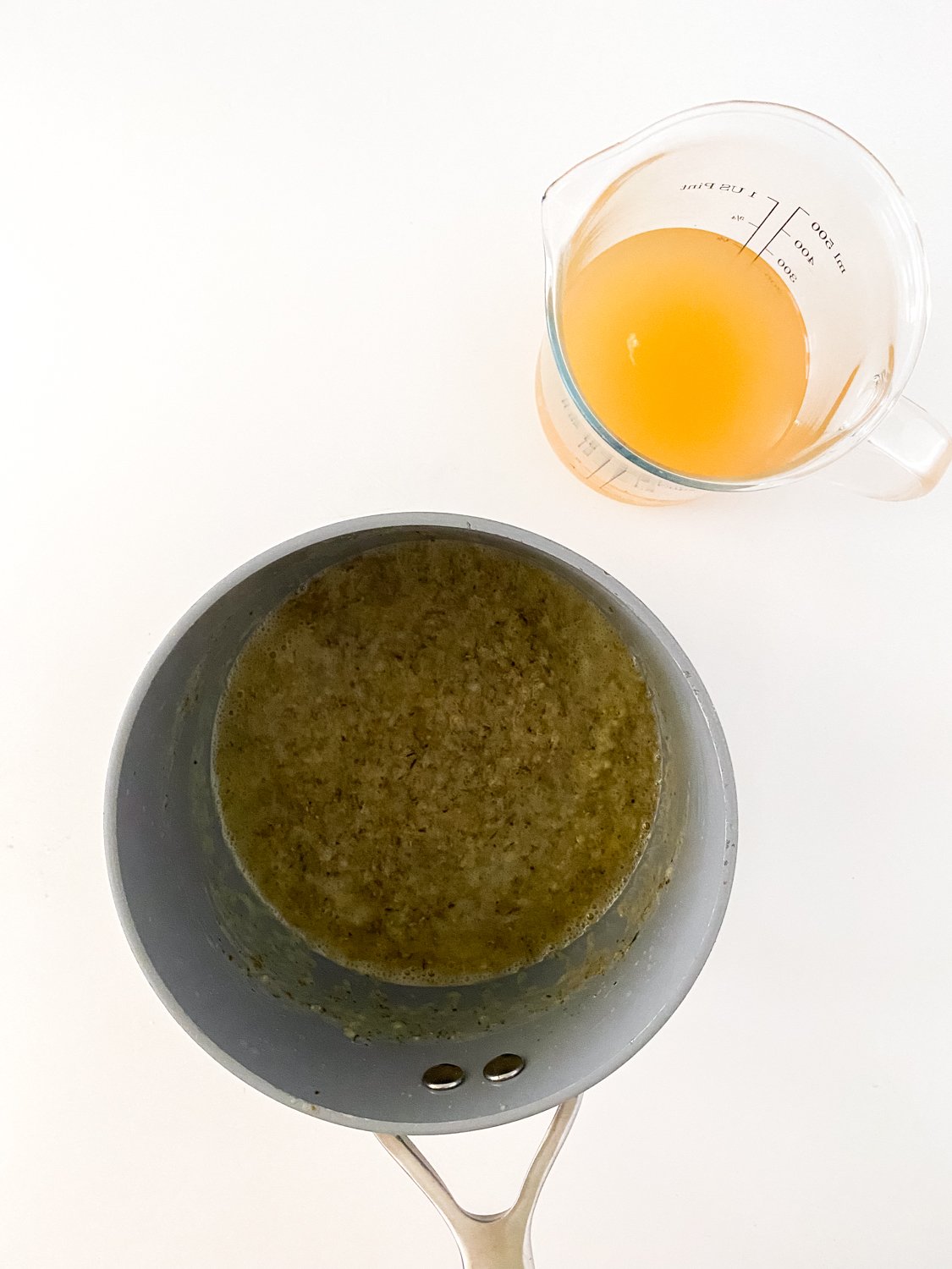 Melted butter mixed with seasonings in a pot. A glass measuring cup sits next to it with broth