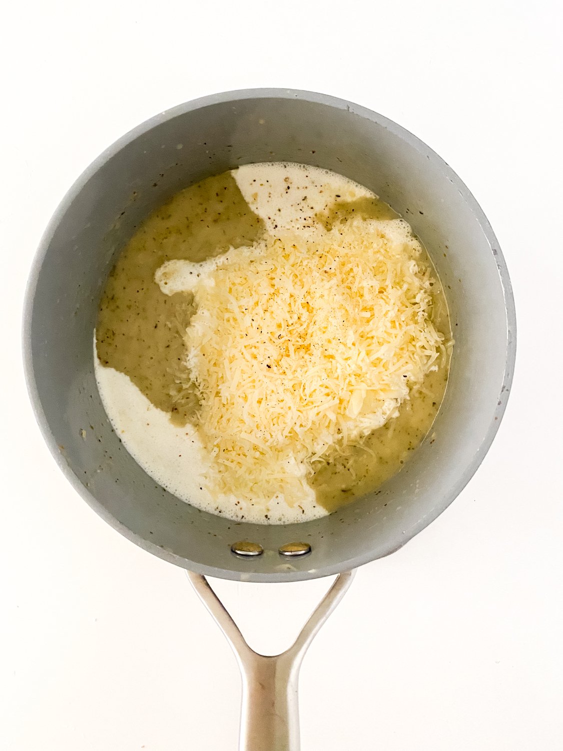 Cream and parmesan cheese are added into the pot of melted butter and seasoning