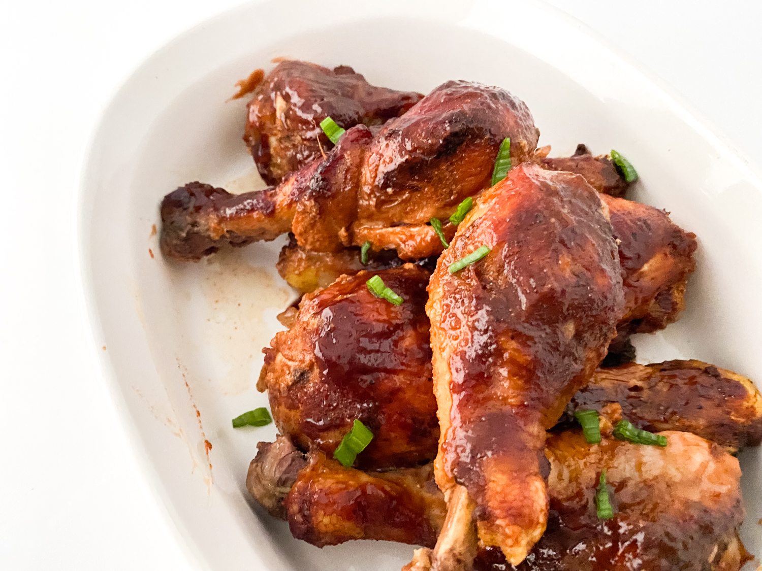 Cooked and garnished gluten free bbq chicken drumsticks on a white serving plate