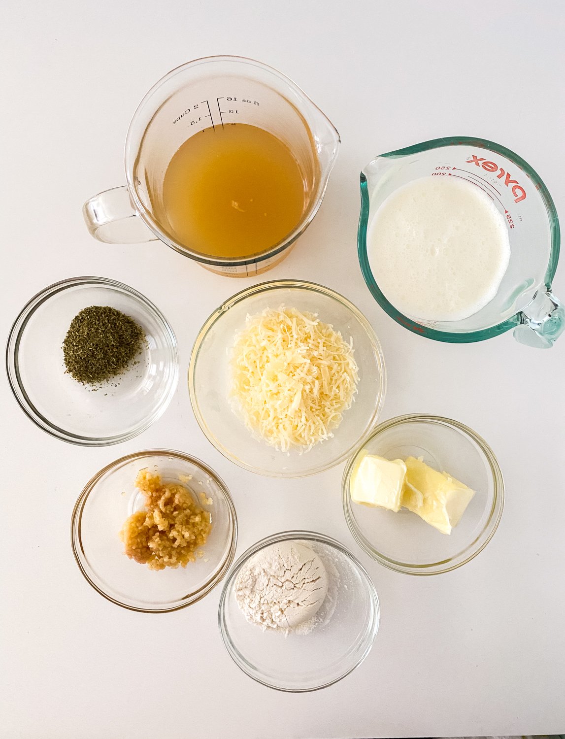 Each of the ingredients for gluten free garlic parmesan sauce is sitting in a glass bowl on a white counter