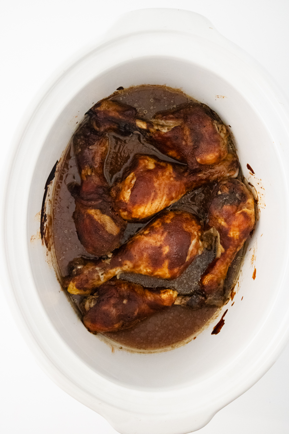 Saucy cooked chicken drumsticks in the bottom of a white slow cooker